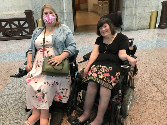 Katie Shelley and Renee Wood, both wheelchair users in floral dresses, pose together