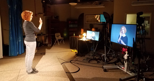 Molly Estes stands in front of video monitors and a TelePrompTer as she signs for DRO's ASL video project