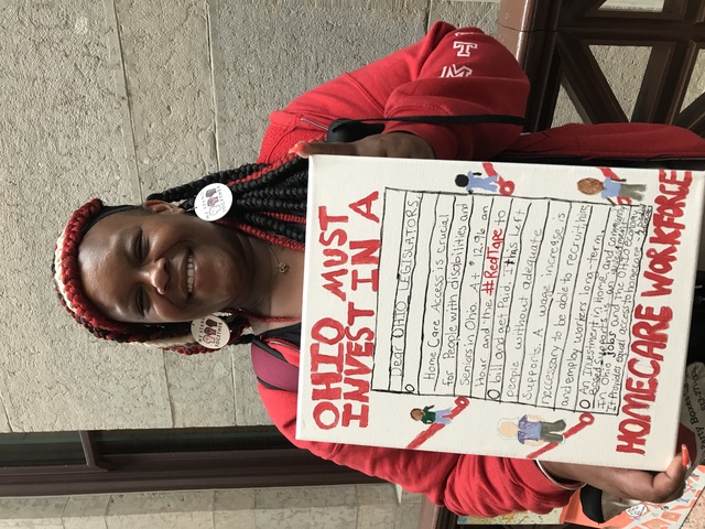 Tracey Mosby holding a piece of Alicia Hopkins's artwork, which depicts home care workers and a letter, and says 'Ohio Must Invest In A Homecare Workforce'