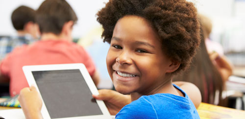 A girl smiles as she holds a tablet in her classroom at school
