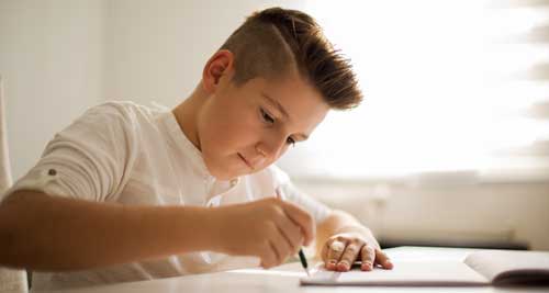 A middle school boy with spiked hair works in a notebook with a pencil and ruler