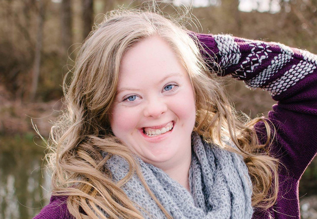 Morgan poses with her hand on her head and a big smile wearing a gray knit scarf and a purple cardigan