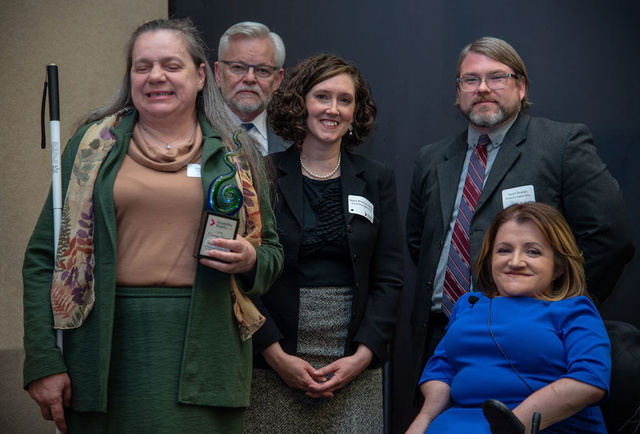 Shelbi Hindel holds her white cane and her DRO Courage Award alongside DRO staff members Michael Kirkman, Stacy Brannan-Smith and Jason Boylan, and Commissioner Julie Hocker, who gave the keynote address