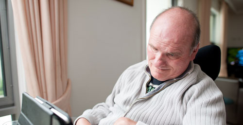 A white man with disabilities looks down as he uses his assistive technology device