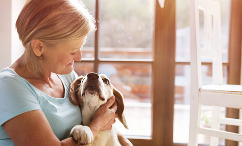 An older white woman with short blonde hair looks down as she cuddles her hound dog