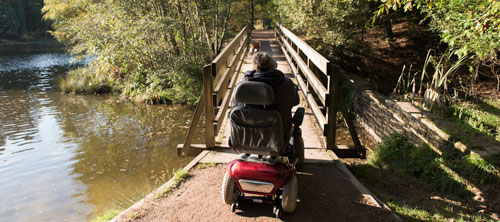 A woman drives her power wheelchair over a footbridge on a lake