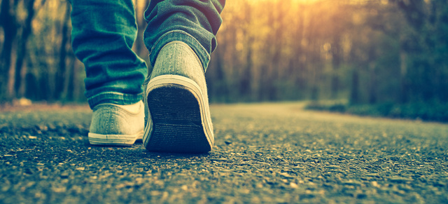 A close-up shot of a woman's feet wearing gray tennis shoes, walking away down a road in the woods